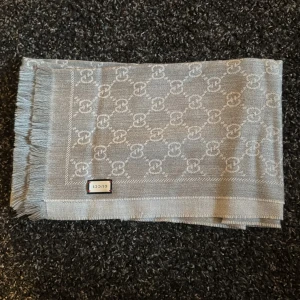 Gucci Halsduk/scarf - Säljer en äkta Gucci halsduk i ull, klassisk grå färg. Stilren, lyxig och perfekt för höst/vinter.  ✅ 100% ull – mjuk och varm ✅ Gucci-mönster, tidlös design ✅ Färg: Grå ✅ Nypris: ca 4 800 kr ✅ I nytt fint skick