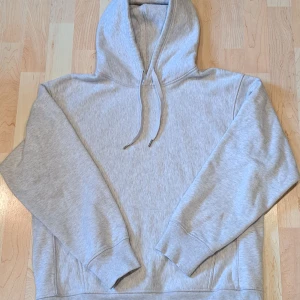 Ljusgrå oversized hoodie från ARKET - En stilren hoodie från ARKET i storlek S. Tröjan har huva med snörning, ribbade muddar och en klassisk känguruficka framtill. Perfekt för chill dagar eller när du vill ha en enkel och clean look. Finns en liten defekt på ena armen men syns knappt därav det billigare priset. Skriv om det är något!