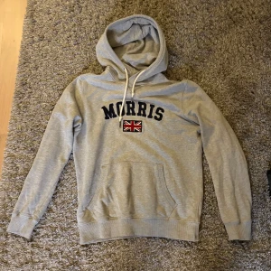 Morris hoodie - Snygg grå hoodie från Morris med svart broderad logga och brittisk flagga på bröstet. Storlek M. Perfekt inför hösten.