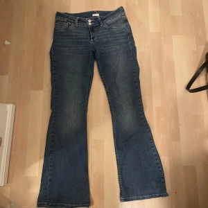 Blå bootcut jeans med broderade fickor - Snygga blå jeans med bootcut passform. Baksidan har broderade detaljer på bakfickorna . Jeansen är low waist och har ett stretchigt material