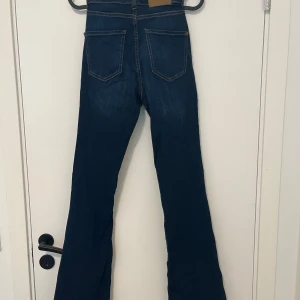 Mörkblå bootcut jeans från Happy Holly - Snygga mörkblå jeans från Happy Holly med bootcut passform och hög midja. Jeansen har klassiska bakfickor, kontrastsömmar och är tillverkade i stretchigt denimtyg för en bekväm känsla. Perfekta för dig som gillar en retroinspirerad look.