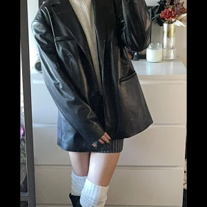 Svart oversized skinnkavaj  - Säljer en svart oversized kavaj i skinnimitation. Jackan har klassisk krage, två knappar framtill och fickor på sidorna. Snygg och trendig look med lång ärm och slät finish. Perfekt nu till hösten. Använd fåtal gånger, säljer för den känns för stor.