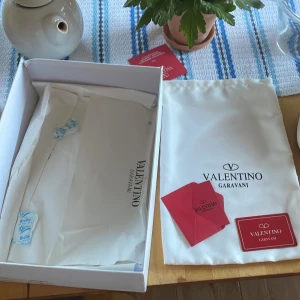 Valentino Garavani Open sneakers vit/blå - Snygga Valentino Garavani Open sneakers i vitt skinn med bred blå rem över vristen. Klassisk rund tå, vita snören och diskret logga på plösen. Kommer med originalkartong, dustbag och äkthetskort. Perfekta för dig som vill ha en lyxig och stilren sneaker.knappt använda bara lite lätt skitiga!