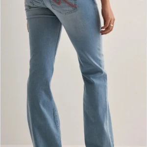 Ljusblå bootcut jeans med broderi - Säljer ett par ljusblå bootcut jeans med snyggt rött broderi på bakfickorna. Jeansen har klassisk femficksdesign, normal passform och är tillverkade i mjukt denimtyg. Perfekta för dig som gillar en avslappnad men trendig look.