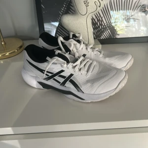 Vita Asics sneakers med svarta detaljer - Säljer ett par fräscha vita Asics sneakers med svarta detaljer och snörning. Skorna har en sportig vibe med meshpaneler för extra andningsförmåga och en rejäl sula som ger bra grepp. Perfekta för dig som gillar stilrena och bekväma skor till träning eller vardag.Bara använd 1-2 gånger!!