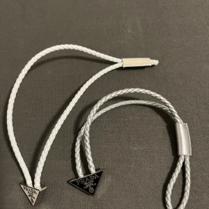 Prada armband i flätat läder - Två stilrena armband från Prada i flätat läder, ett i vitt och ett i silver. Båda har den ikoniska trekantsloggan i metall med texten 'PRADA MILANO'. Perfekt accessoar för att lyfta din outfit med en lyxig touch.