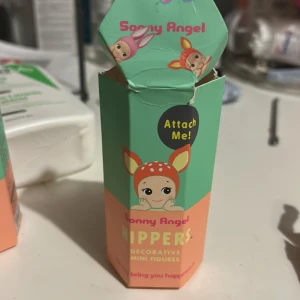 Sonny Angel Hippers Decorative Mini Figure - Sonny Angel Hippers är en dekorativ mini-figur med rosa kaninöron, perfekt att fästa på olika ytor. Figuren och förpackningen är i mycket gott skick, endast öppnad för visning. Samlarobjekt och rolig dekoration för skrivbord eller hylla.