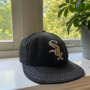 Svart White Sox keps från New Era - Snygg svart keps från New Era 59FIFTY med vit White Sox-logga framtill och vita kontrastsömmar. Klassisk basebollmodell med böjd skärm och broderade detaljer. 