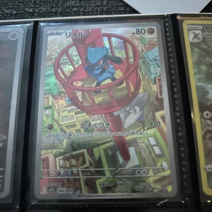 リオル (Riolu) - Coolt japanskt Pokémonkort med Riolu i färgglad stadsmiljö. Perfekt för samlare och fans av Pokémon! Kortet har snygg design och är en unik del av din samling.