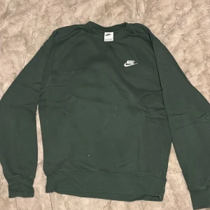 Mörkgrön Nike sweatshirt i bomull - Mörkgrön sweatshirt från Nike med klassisk logga broderad i vitt på bröstet. Tröjan har rund hals, långa ärmar och ribbade muddar vid ärmslut och nederkant. Perfekt för en chill och sportig stil.