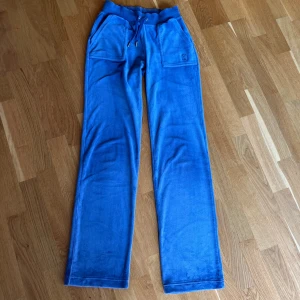 Blå mjukisbyxor Juicy Couture XS - Blå mjukisbyxor från Juicy Couture i supermjuk fleece. Byxorna har bred resår i midjan med snörning, stora fickor fram och bak med knappdetaljer samt broderad logga på ena fickan. Perfekt för en chill och trendig look. De är tidigare köpta här på Plick. Tveka inte om att fråga om du har frågor!💕