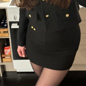 Svart minikjol med guldknappar - Stilren svart minikjol med två  guldknappar framtill. Kjolen är en kort modell och passar till det mesta💜