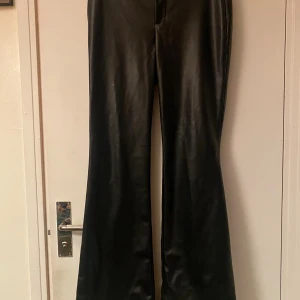 Svarta bootcut byxor i skinnimitation Zara - Snygga svarta byxor från Zara i skinnimitation med bootcut-modell. Byxorna har en hög midja och en stilren, slät yta. Perfekta för dig som vill ha en edgy look med lite extra attityd.