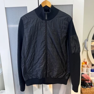 J.Lindeberg hybrid jacka / cardigan - Jätte fin J.Lindeberg Beck knitted hybrid jacket  Storlek L på lappen Jackan är i jätte bra och fint skick Svart färg med svart logga på vänster sida arm Skicka meddelande vid några funderingar  Kolla gärna även in mina andra annonser