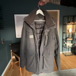 Grå dunjacka från Sail Racing - Säljer en grå dunjacka från Sail Racing med quiltad insida och hög krage. Jackan har flera praktiska fickor med dragkedja och en stilren design. Perfekt för kalla dagar och har en snygg mörkgrå ton. Passar dig som gillar funktion och stil.