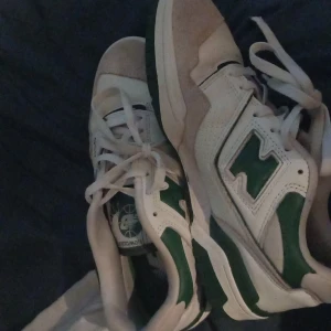 New Balance 550 vit/grön sneaker - Säljer ett par New Balance 550 sneakers i vitt och grönt. Skorna har klassisk retrodesign med gröna detaljer, perforerad ovandel i skinn och mocka vid tån. Låg modell med snörning och platt sula, perfekt för dig som gillar streetstyle och sportig vibe.