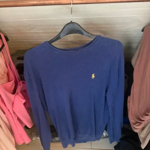 Blå pullover tröja från Polo Ralph Lauren - Snygg blå pullover tröja från Polo Ralph Lauren med klassisk gul logga broderad på bröstet. Skön modell som funkar året runt. Sitter mer som S än M. Toppen skick
