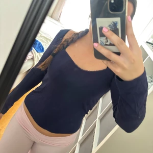 Mörkblå långärmad topp med spetskant - Säljer en mörkblå långärmad topp med söt spetskant runt den fyrkantiga urringningen. Toppen är figurnära och har en enkel, stilren design som passar perfekt till jeans eller kjol.