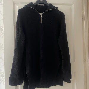 Svart stickad tröja med half zip - Svart stickad tröja från med halv dragkedja vid kragen. Tröjan har lång ärm, ribbad struktur och en lite lösare passform. Perfekt för lager-på-lager under kyliga dagar.