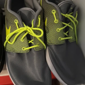 Nike sneakers grå och neongula - Snygga Nike sneakers i grått med neongula detaljer och snörning. Ovandelen har ett stickat mönster i grått och gult, medan sulan är vit. Perfekta för dig som gillar sportig stil och vill sticka ut med färg. Sköna och lätta på foten.