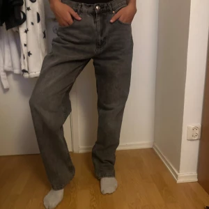 Grå raka jeans med loose fit - Säljer ett par grå jeans med rak passform och loose fit. Byxorna har klassisk femficksdesign, bälteshällor och knappgylf. Perfekta för dig som gillar en avslappnad och trendig look. Materialet är jeans och färgen är en snygg mörkgrå ton.
