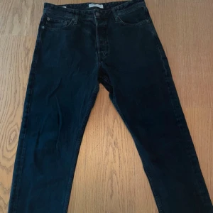 Svarta jeans från Jack & Jones - Svarta jeans från Jack & Jones med klassisk femficksdesign och raka ben. Jeansen är tillverkade i bomull och har en snygg, enkel look som passar till det mesta. Stängs med knapp och dragkedja framtill. Perfekta för dig som gillar stilrena och bekväma jeans.
