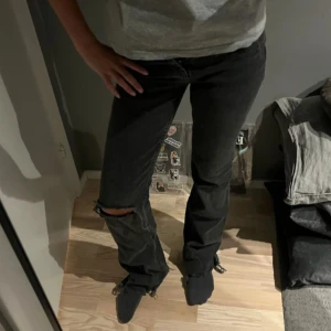 Svarta jeans med slitning på knät - Svarta jeans från Gina tricot med rak passform och slitning på ena knät. Jeansen har klassisk femficksdesign och är tillverkade i denim. Perfekta för en avslappnad och trendig look.