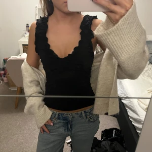 Svart croppad linne med volang - Säljer ett skitsnygg svart croppat linne med lite bredare band med volanger. Den är helt oanvänd och köpte för 249kr.