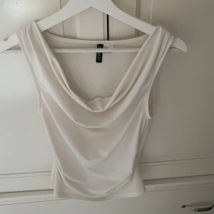 Vit draperad linnetopp från H&M - Säljer en vit linnetopp från H&M med snygg draperad halsringning. Toppen är ärmlös och har en mjuk, följsam känsla i ett slätt material. Perfekt att styla med jeans eller kjol för en fräsch look.