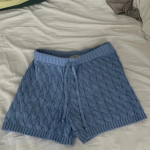 Blå stickade shorts Sanne Alexandra XS - Säljer ett par ljusblå stickade shorts från Sanne Alexandra i storlek XS. De har ett snyggt kabelstickat mönster, ribbad midja med snörning och är riktigt mjuka och sköna. Perfekta för chill dagar hemma eller när du vill ha en cozy vibe. Aldrig använda.