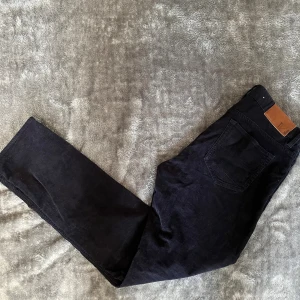 Mörkblåa manchesterbyxor från T/J - Snygga mörkblåa manchesterbyxor från T/J med klassisk femficksdesign och läderpatch bak i midjan. Byxorna har raka ben och är tillverkade i mjuk manchester som ger en cool och tidlös look. Perfekta för dig som gillar stilrena och bekväma byxor.