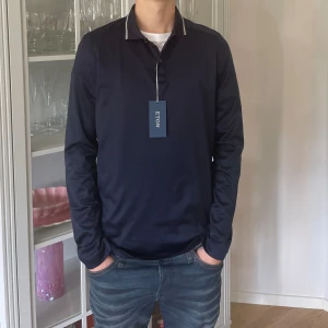 Mörkblå långärmad Pikétröja från Eton (Helt Ny) - Jag säljer den här mörkblåa långärmade pikétröjan från Eton i storlek S. Den är helt ny med etiketten kvar. Nypris ligger på 1700kr och jag säljer den här för 600kr. Tveka inte att höra av er!