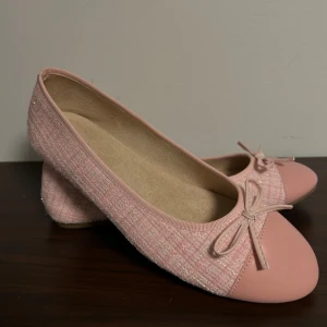 Rosa ballerinaskor med rosett, stl 41 - Söta ballerinaskor i ljusrosa med glittrig textil och matchande rosa tåparti i syntet. Skorna har en dekorativ rosett framtill och en platt sula. Perfekta för dig som gillar en feminin och chic stil.