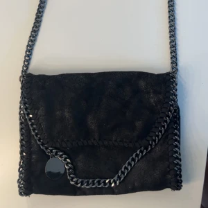 Svart axelväska - Snygg svart axelväska med grova silverfärgade kedjor längs kanterna och som axelrem. Väskan har ett lock och insidan är fodrad med leopardmönster.