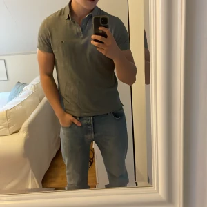 Grå pikétröja från Tommy Hilfiger - Säljer en stilren pike som är använd runt 10-15 ggr, säljer pga att jag växt ur den     Jag är 185cm och väger 90kg Nypris: 1100kr