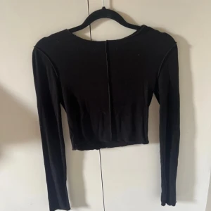 Svart croppad långärmad topp Zara - Svart croppad långärmad topp från Zara med råa kanter och synlig söm mitt bak. Säljes i storlek S.