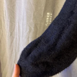 Svart fluffig stickad tröja Divided - Mysig svart stickad tröja från Divided med fluffig känsla. Tröjan har en avslappnad passform och långa ärmar med lätt ballongeffekt. Perfekt för kyliga dagar och enkel att styla med jeans eller kjol.