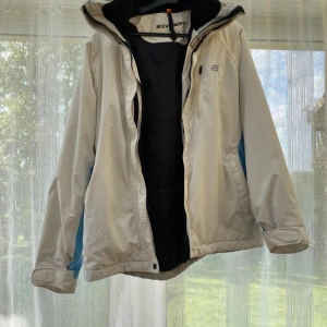 Vit vindjacka från Everest, strl 38 - Säljer en vit vindjacka från Everest i storlek 38. Jackan har dragkedja framtill, huva och diskreta blå detaljer i sidorna. Dragkedjan funkar inte som den ska men går att laga. Nypris är runt 1000kr