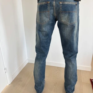 Blå jeansbyxor från tramarossa - Snygga blå jeansbyxor från tramarossa med klassisk femficksdesign, orange kontrastsömmar och detaljer som broderad logga på myntfickan. Jeansen har en rak passform och är tillverkade i mjukt denim med lätt tvättad look och italienska flaggan på insidan av linningen.
