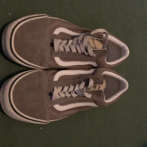 Gråa Vans Old Skool sneakers - Säljer ett par klassiska Vans Old Skool sneakers i grå mocka och textil med vit sula och vit sidostrip. Skorna har snörning och en låg profil, perfekt för en avslappnad streetstil. Ikonisk design med rund tå och platt sula.