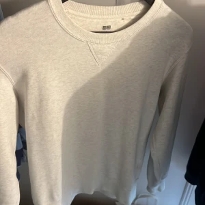 Vit sweatshirt från Uniqlo - En stilren vit sweatshirt från Uniqlo med klassisk rund halsringning och ribbade muddar. Tröjan är långärmad och tillverkad i mjuk bomull, perfekt för lager-på-lager under kyliga dagar. Enkel och clean design som funkar till allt.
