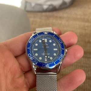 Omega Seamaster  - Omega Seamaster med blå urtavla och vågmönster, silverfärgat mesharmband i metall och blå vridbar bezel. Klockan är 38 mm men sitter väldigt snyggt på handleden. Klockan är i väldigt fint skick. Tveka inte att skriva till mig om frågor!