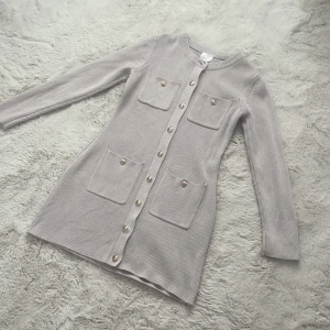 Klänning - En jätte snygg och elegant beige klänning från H&M. Klänningen har guldiga knappar som ger en väldigt stilren look. Den är endast använd en gång och är i jätte bra skick. Den är i storlek S men passar som M då den är större i storlek.