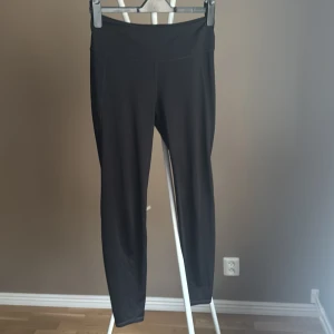Svarta yoga byxor sport - Svarta leggings i ett stretchigt och mjukt syntetmaterial. De har hög midja och en tight passform som sitter skönt mot kroppen. Perfekta för träning eller chill dagar. Snygg och enkel design utan synliga loggor eller detaljer.