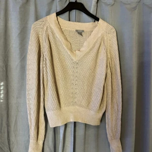 Beige stickad tröja från Lindex - Superfin beige stickad tröja från Lindex med v-ringad hals och breda muddar. Tröjan har en loose passform och är perfekt att slänga på sig när det är lite kyligare ute. Snyggt stickat mönster och långa ärmar ger en avslappnad vibe.
