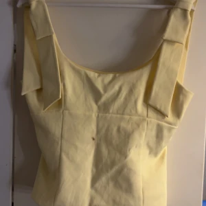 Gul topp med rosettband från Zara - Säljer en super söt Gul blus från Zara i storlek M. Den är ganska små i storleken så skulle säga att den passar perfekt då för nån med storlek S/XS. Den är helt oanvänd men har fått nån fläck men jag tvättar såklart innan. 💗💗