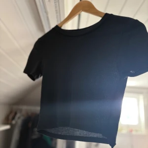 Svart ribbad croppad topp från Zara - Svart croppad topp från Zara med rund halsringning och korta ärmar. Toppen är ribbad och har en tight passform som sitter snyggt på kroppen. Perfekt att matcha med jeans eller kjol för en clean look.