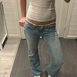 Bootcut jeans från Nelly, ljusblå - Säljer ett par ljusblå bootcut jeans från Nelly i modellen 'No Waist Bootcut Jeans'. De har låg midja, rå kant upptill och klassisk femficksdesign. Jeansen är i mjuk denim och har en avslappnad passform med utsvängda ben.