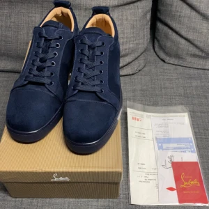 Mörkblå sneakers från Louboutin - Snygga mörkblå sneakers från Christian Louboutin i mocka med klassisk röd sula och diskret broderad logga på hälen. Skorna har rund tå, snörning och en stilren design som passar perfekt till jeans eller dressade outfits.