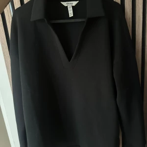 Svart långärmad tröja från Spanx - Svart långärmad tröja från Spanx med krage och djup v-ringning. Tröjan har en clean och stilren look med lite loose passform och är tillverkad i en mjuk mix av modal, polyester och elastan. Perfekt för dig som gillar minimalistisk stil.